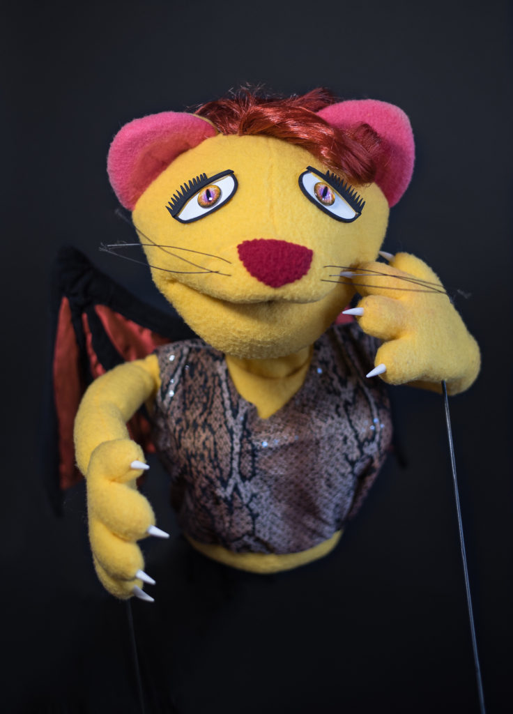 Manticore puppet with yellow skin, big claws, and bronze wings, wearing a snakeskin shirt.